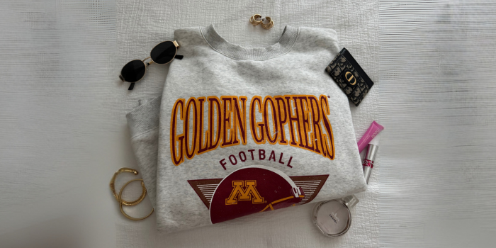 University of Minnesota Merch with sunglasses, a wallet, earrings, and perfume next to it