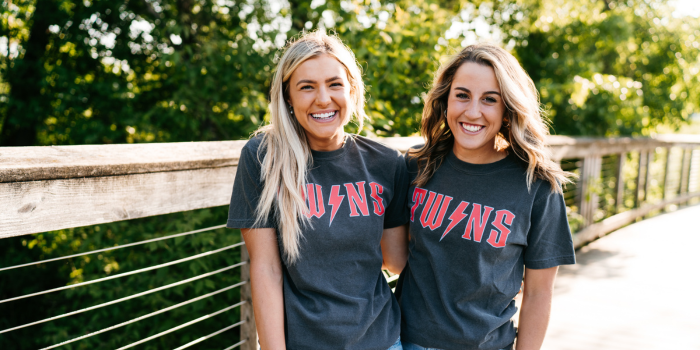 A picture of two girls smiling on a bridge wearing gray t-shirts that say Twins on them