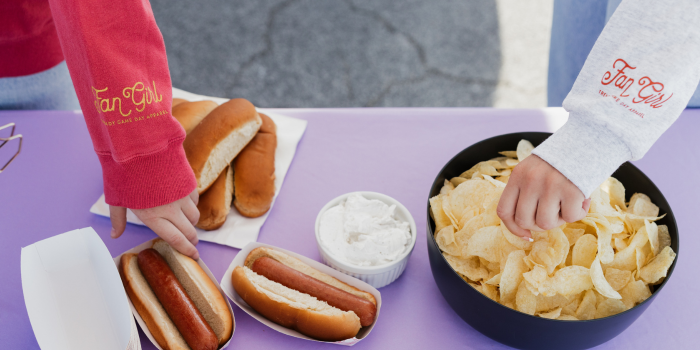 hands going to grab hot dogs and chips on a tailgate snack table