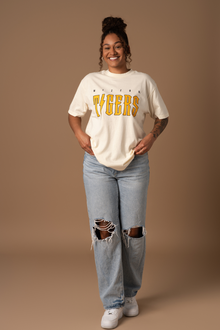 A full body photo of a girl wearing a cream colors vintage t-shirt with an oversized Mizzou Tigers design on the front in black and gold.