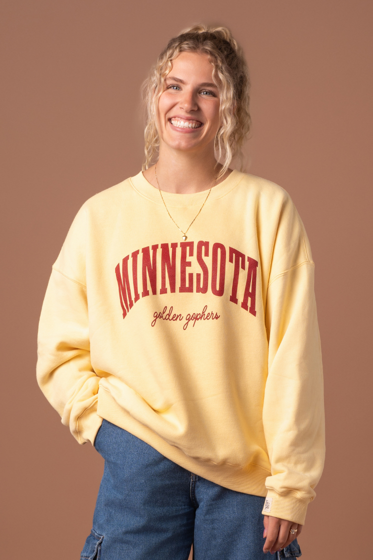 close up image of a girl wearing a butter yellow crewneck with Minnesota Golden Gophers screenprinted in maroon across the chest