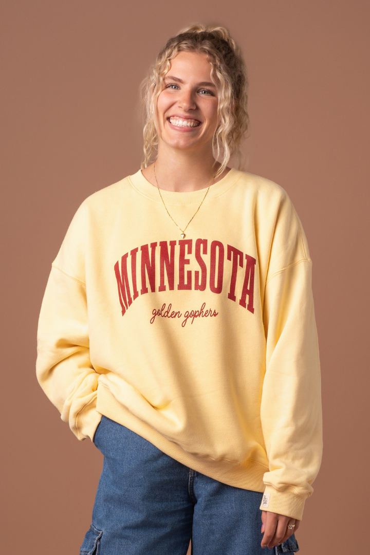 close up image of a girl wearing a butter yellow crewneck with Minnesota Golden Gophers screenprinted in maroon across the chest