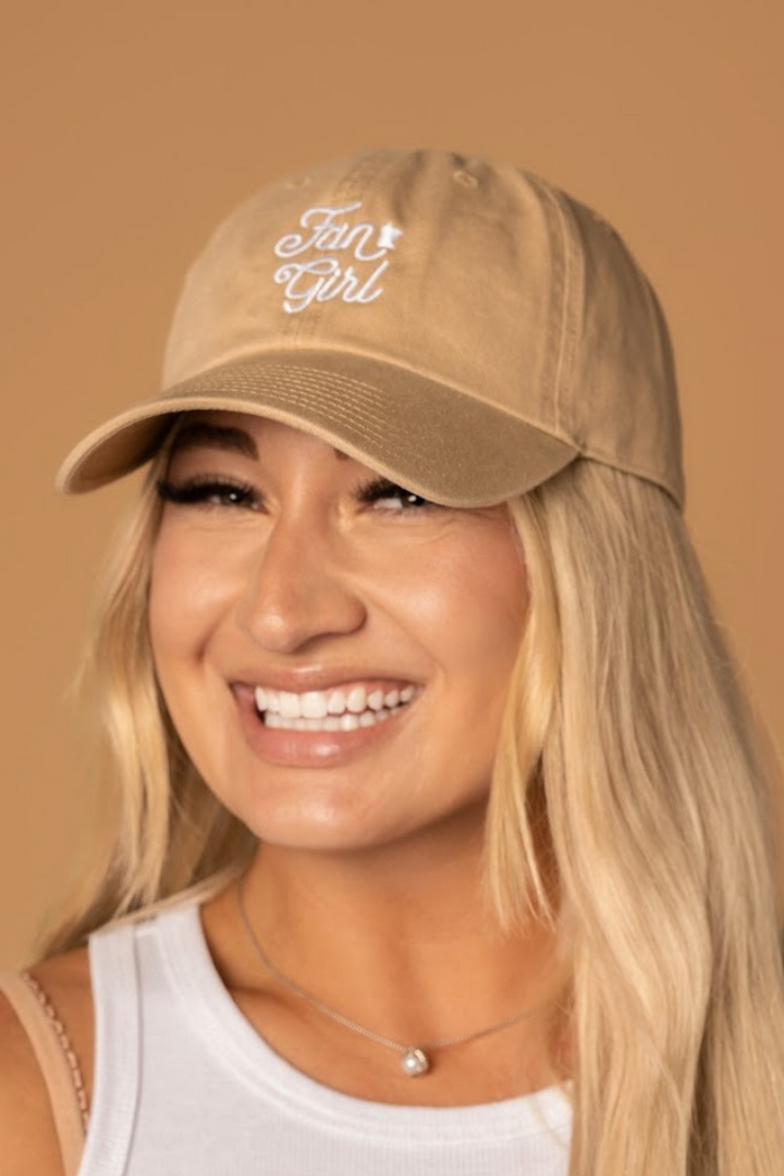 close up picture of a girl wearing a tan baseball hat with a white embroidered Fan Girl logo
