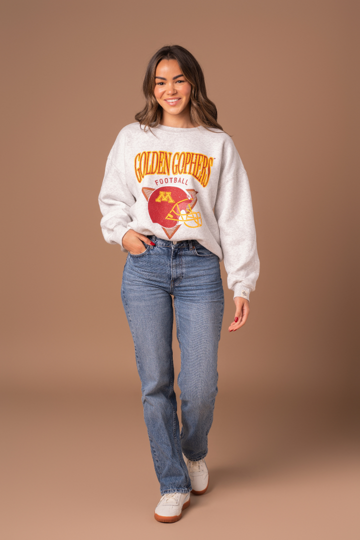 full body image of a girl wearing jeans and an ash gray crewneck with Golden Gophers Football screenprinted with a distressed football graphic in maroon and gold