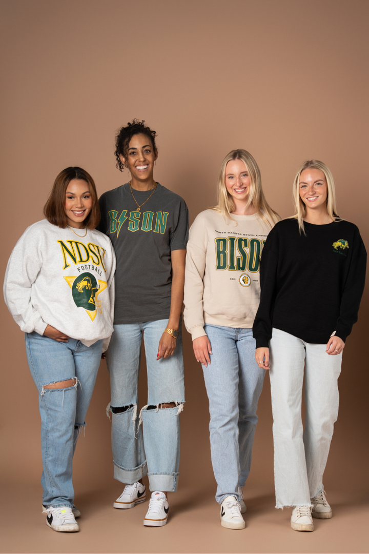 4 girls posing in a line, all of them are wearing a different NDSU Bison style, all of which have green and gold decorations on them