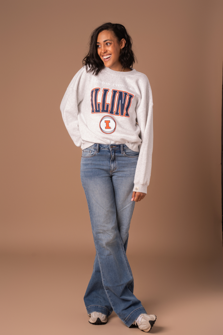 University of Illinois Fighting Illini Crew Neck Sweatshirt full body shot. The sweater has orange, navy blue, and white screen printed detail with licensed Illinois trademarks. Model is wearing jeans and sneakers.
