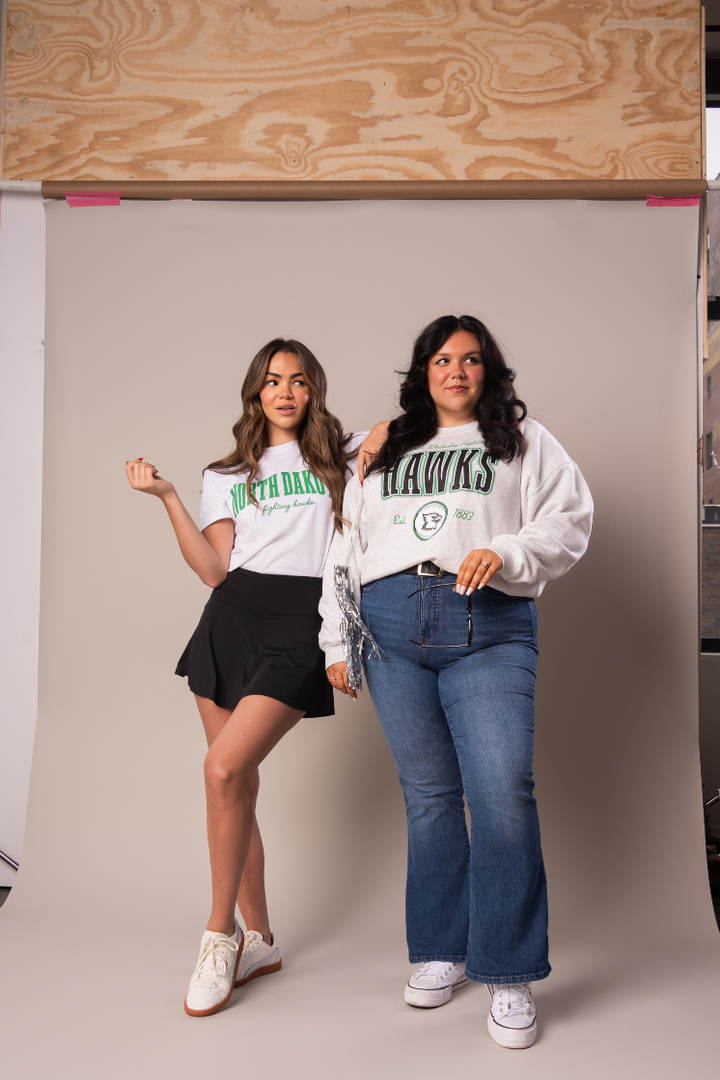 image of 2 girls posing together while one is wearing a North Dakota tee and the other has a Fighting Hawks crewneck on