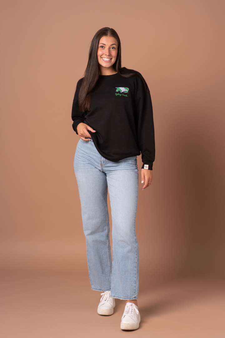 full body image of a girl posing while wearing jeans and black crewneck with a Fighting Hawks logo embroidered on the left side of the crew
