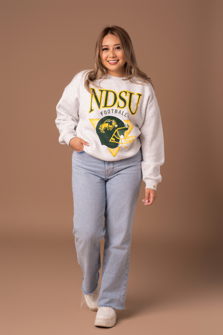 a full body image of a girl wearing jeans and an ash gray crewneck with NDSU logo on a football helmet in green and gold decoration