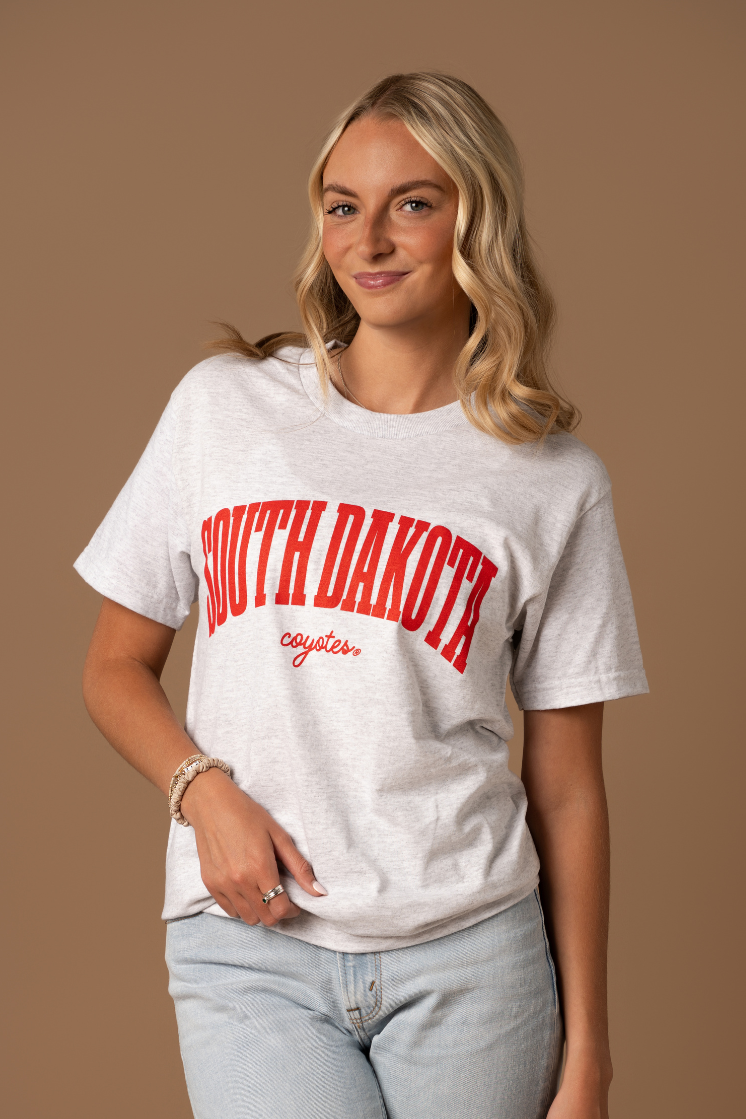 close up image of a girl wearing an ash gray tee with South Dakota Coyotes written in cursive in red
