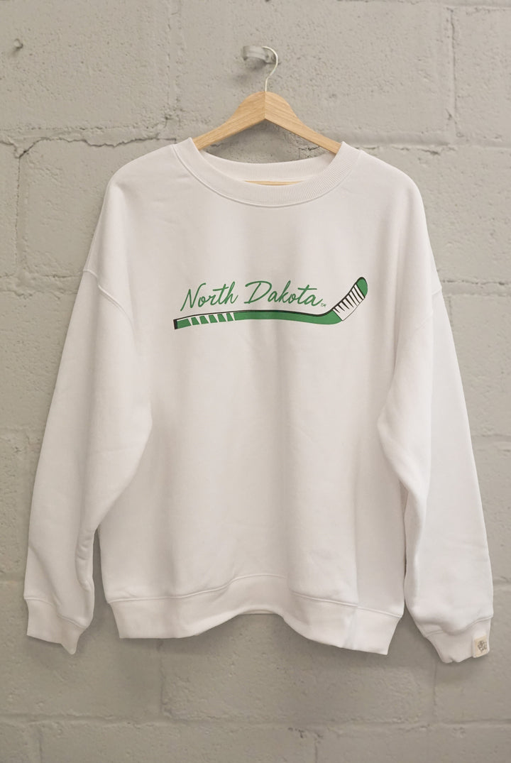 image of a white crewneck on a hanger hanging on a brick wall with North Dakota written in green with a hockey stick graphic on the crewneck