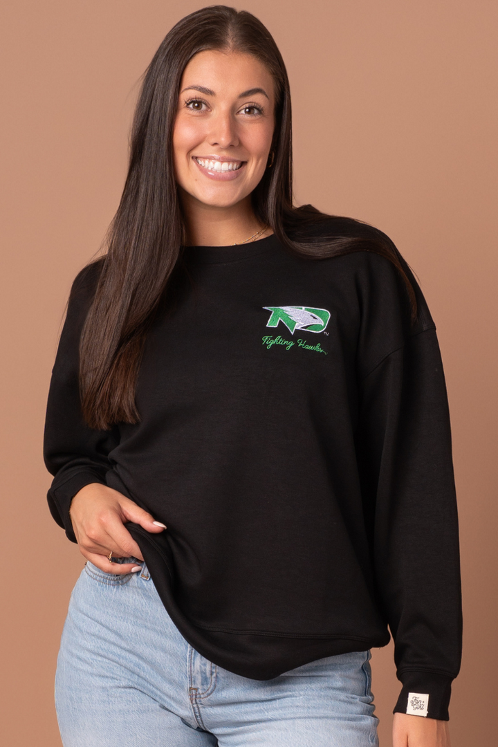close up image of a girl wearing a black crewneck with a UND Fighting Hawk logo embroidered in the left side pocket of the crew