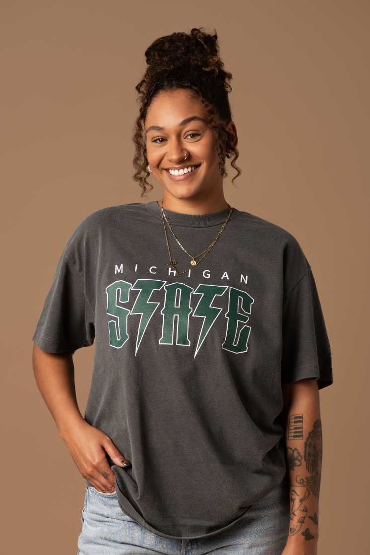 close up picture of a girl wearing a faded black cotton Michigan State Spartans Vintage Band Tee with a green and white screenprinted graphic