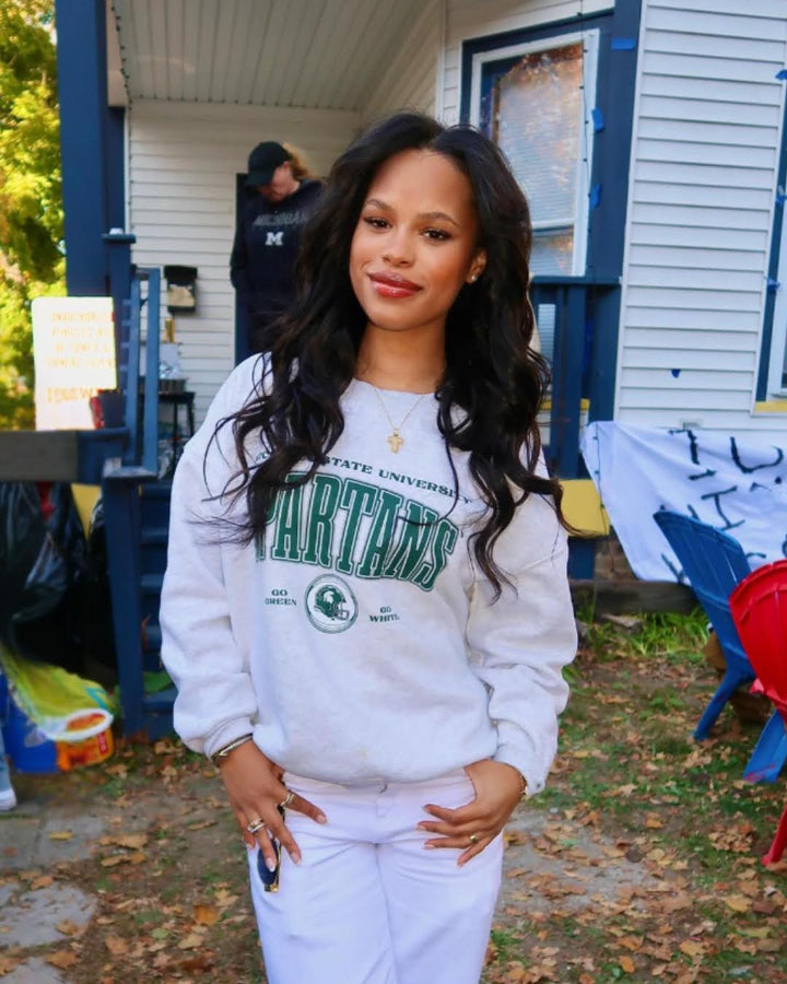 picture of a girl at a tailgate wearing a ash gray fleece lined Michigan State University Vintage Oversized Crew Neck sweatshirt with a green, black, and white screenprinted design
