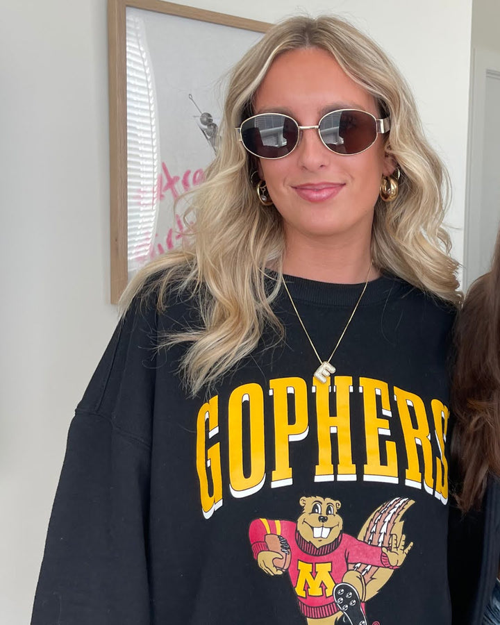 close up image of girl wearing sunglasses, gold jewelry and a black crewneck with Gophers screenprinted in gold across the chest with a Goldy graphic holding a football in maroon and gold decoration