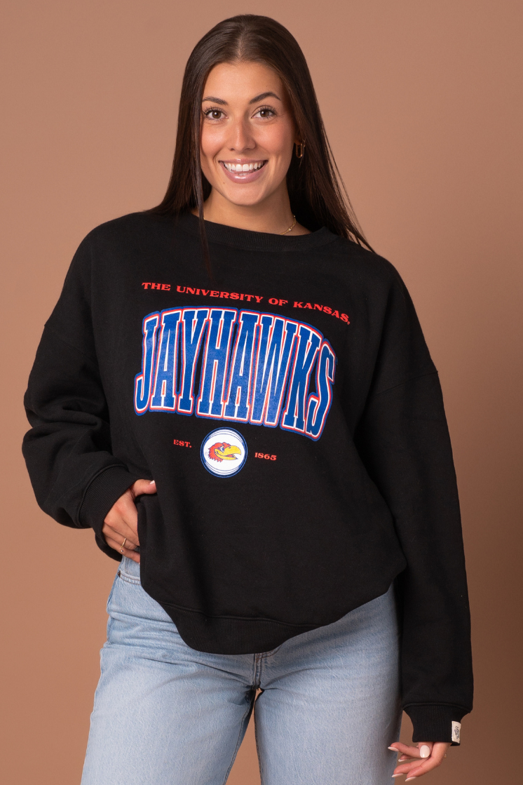close up image of a girl wearing a black crewneck with The University of Kansas Jayhawks screenprinted in red and blue with a Jayhawk logo below