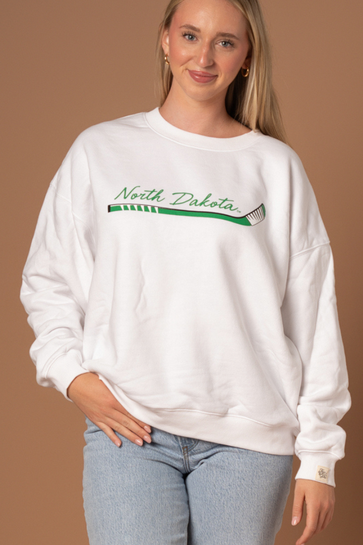 close up of a girl wearing a white crewneck that says North Dakota in kelly green with a green, black and white hockey stick below it