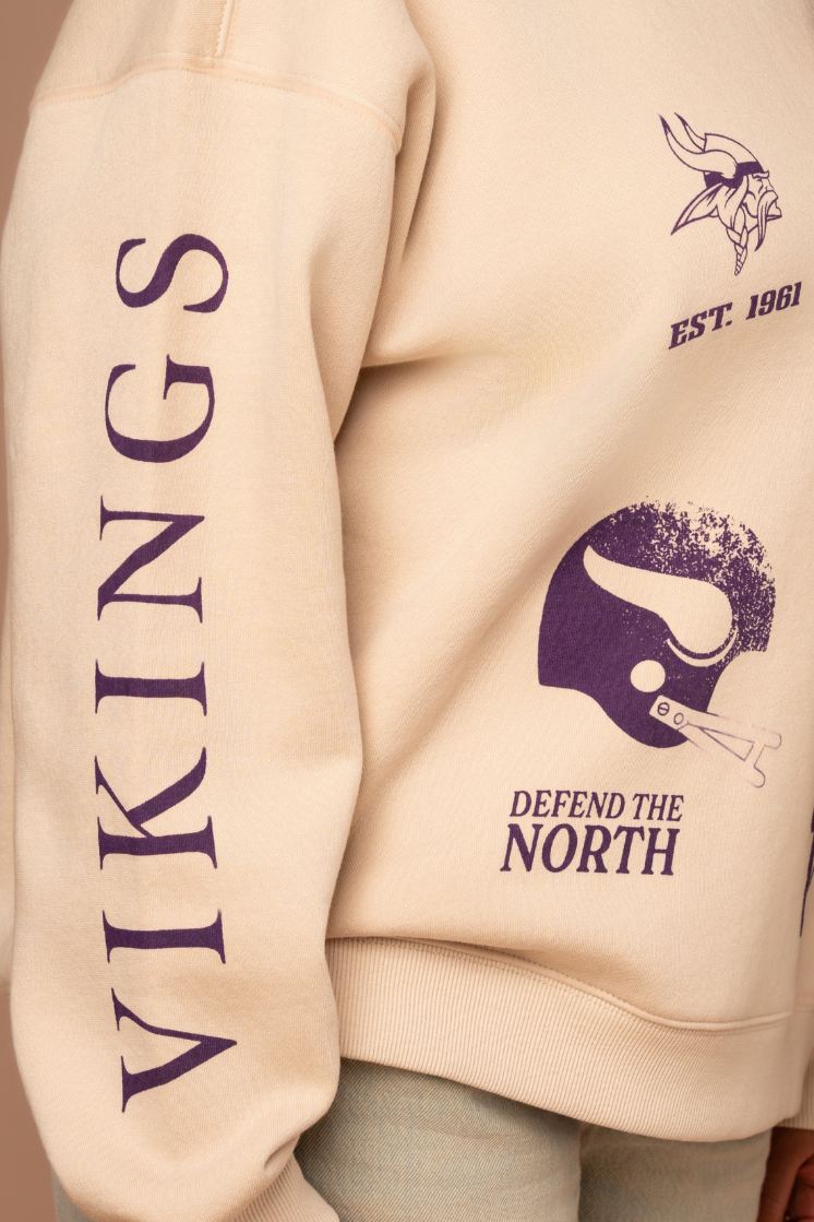 A tan crew neck sweatshirt with five, small purple Minnesota Vikings graphics scattered around the front with purple 'Vikings' text down the arm