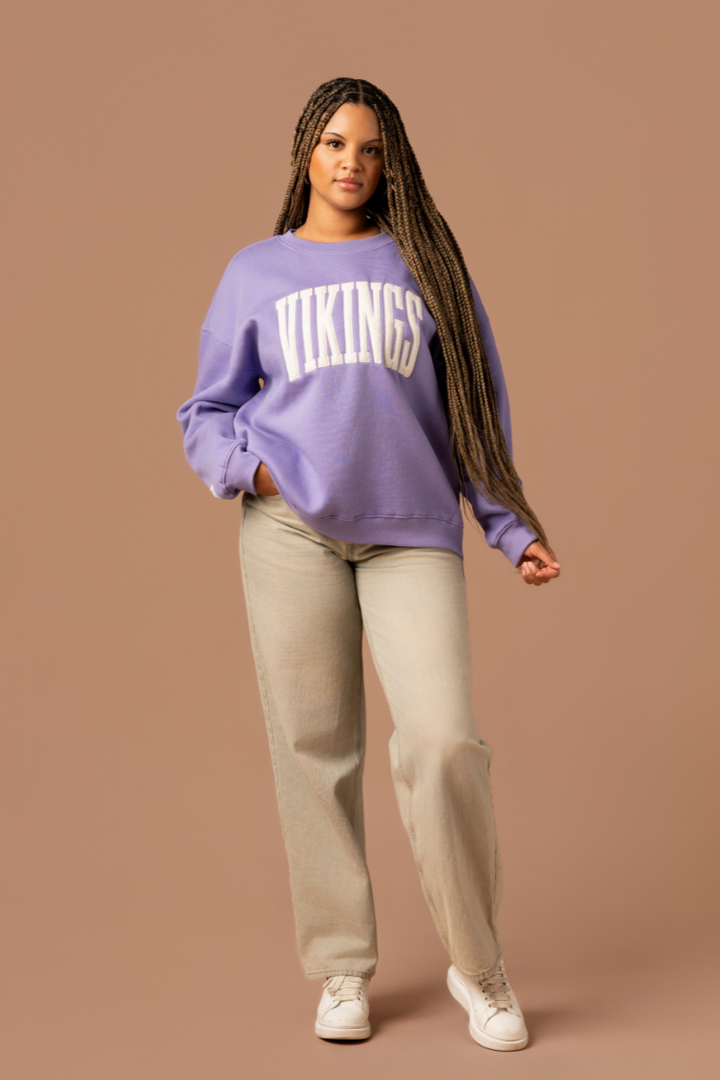 Woman wearing a purple crew neck sweatshirt with large, cream 'Vikings' text