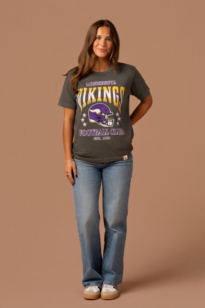 Woman wearing a faded black t-shirt with gold and purple 'Minnesota Vikings Football Club' and 'EST. 1961' text with a purple Vikings helmet graphic in the center