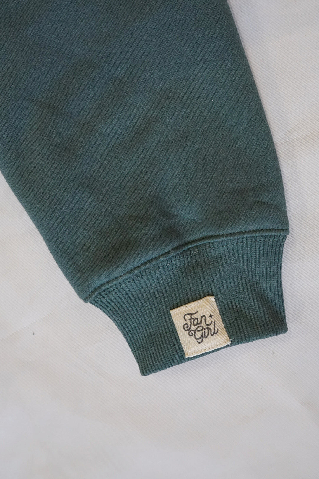 A close up photo of the sleeve and cuff of a sweatshirt with a small Fan Girl logo tag.