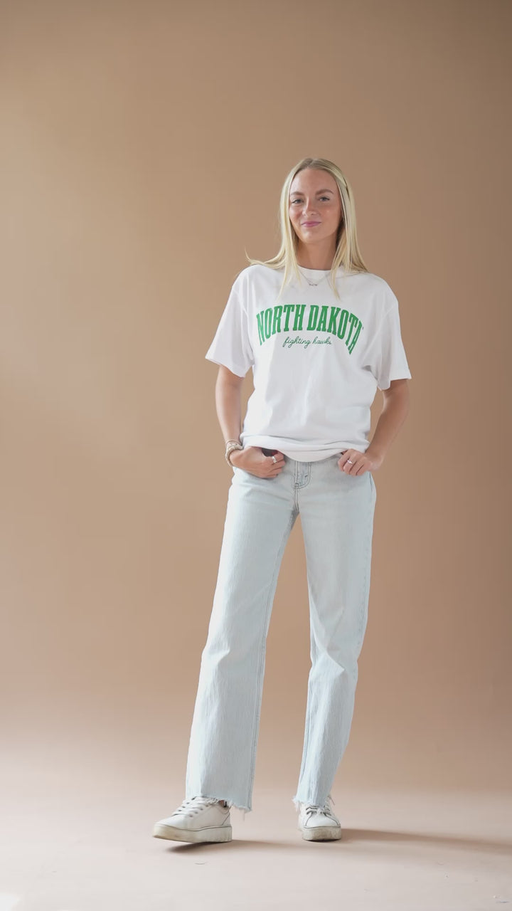 video of a girl dancing and smiling while wearing jeans and a white tshirt with green text that says North Dakota Fighting Hawks