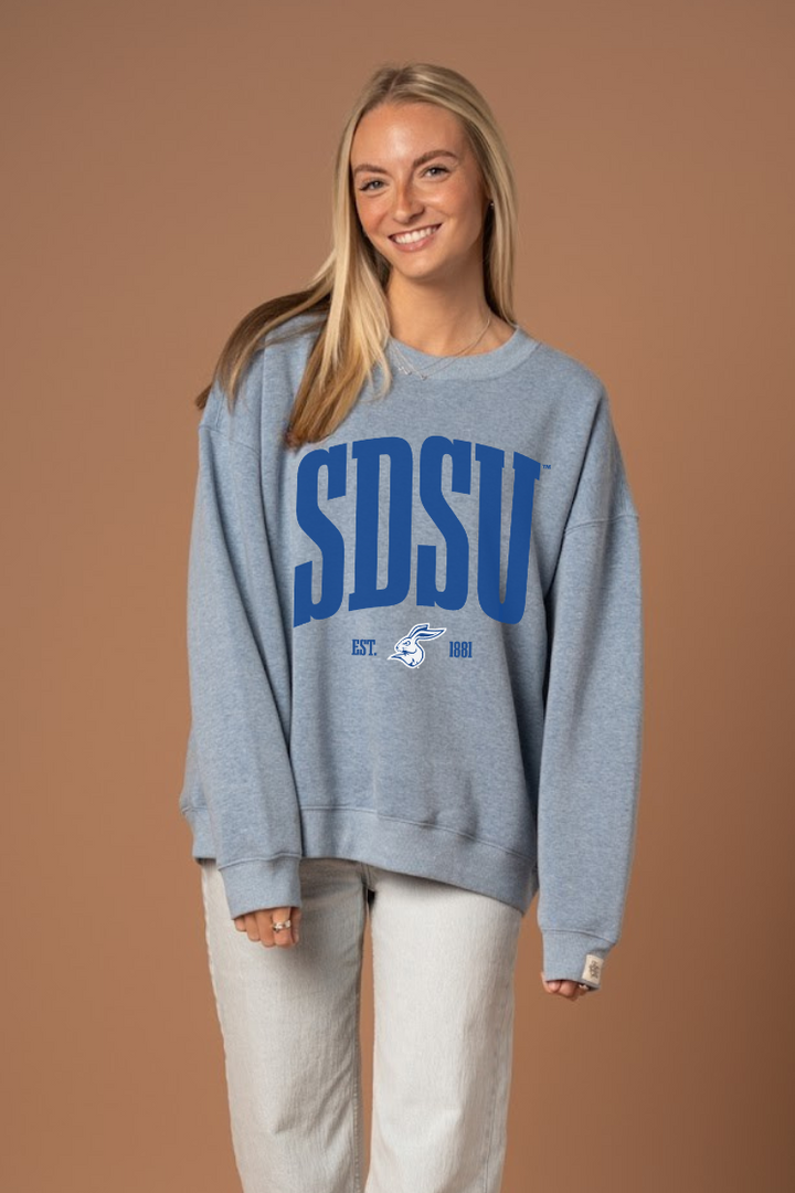 Woman wearing a blue crew neck sweatshirt with darker blue 'SDSU' text and a Jackrabbit logo under it in white