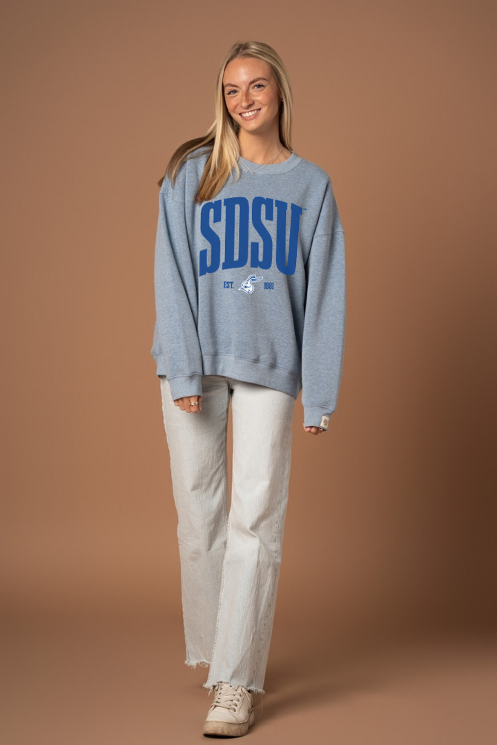 Woman wearing a blue crew neck sweatshirt with darker blue 'SDSU' text and a Jackrabbit logo under it in white