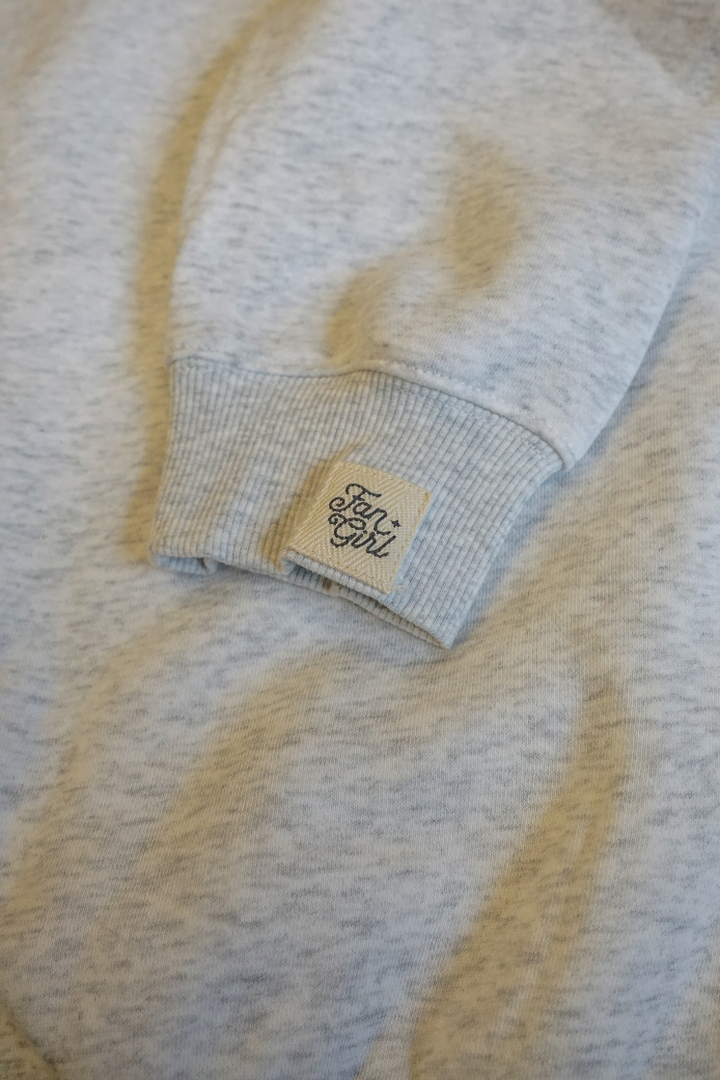 Close-up of a light grey hoodie sleeve with a branded tag