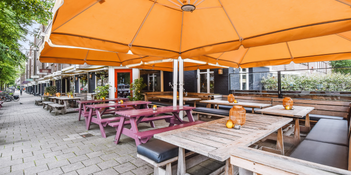 Outdoor restaurant patio with picnic tables and an awning over them 