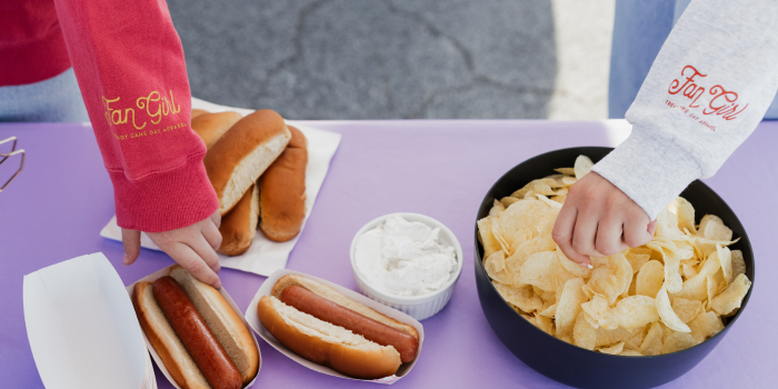 hands going to grab hot dogs and chips on a tailgate snack table 