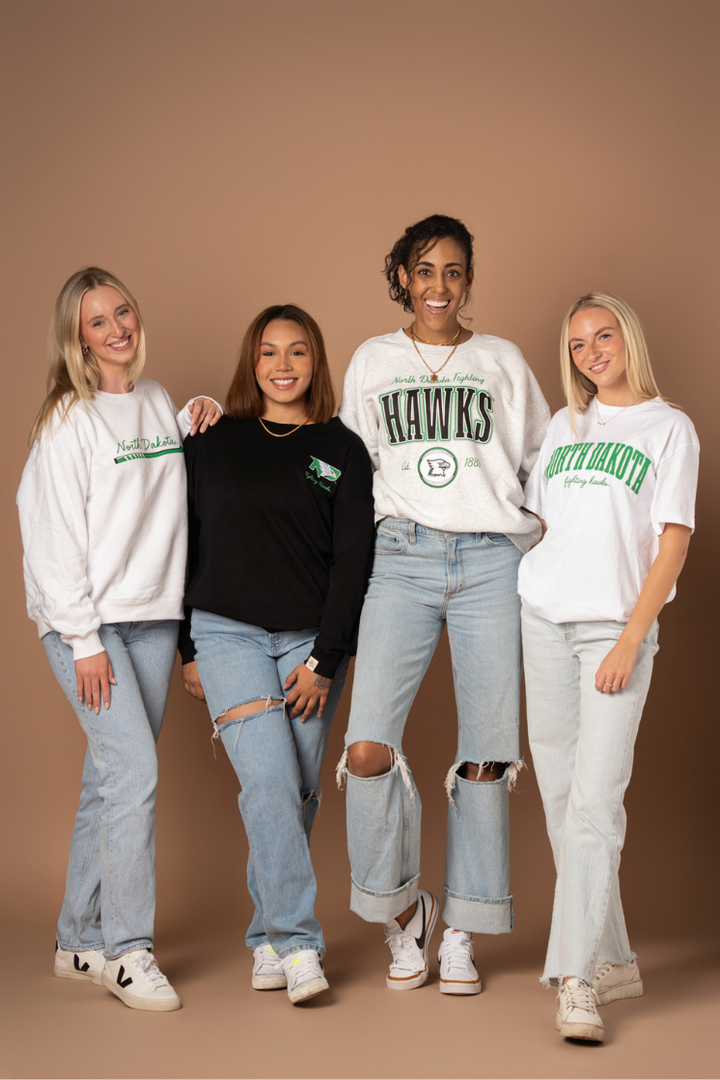 4 girls standing together smiling, all in different UND styles all of which have kelly green decorations