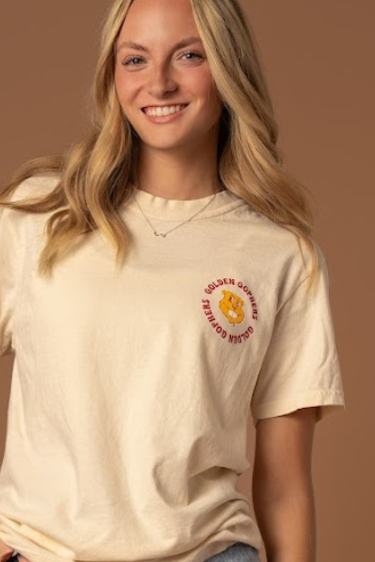 close up image of a girl wearing a cream colored t-shirt with small Goldy head screenprinted in the left pocketside of the tee