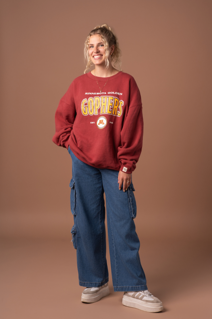 full body image of a girl wearing jeans and a maroon crewneck with Minnesota Golden Gophers screenprinted with a M logo in maroon, gold and white decoration