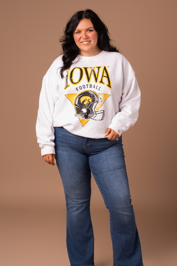 farther away photo of a woman wearing a women's fit, white crew neck sweatshirt. The sweatshirt has black and yellow screenprinted Iowa Hawkeyes football design with a helmet.