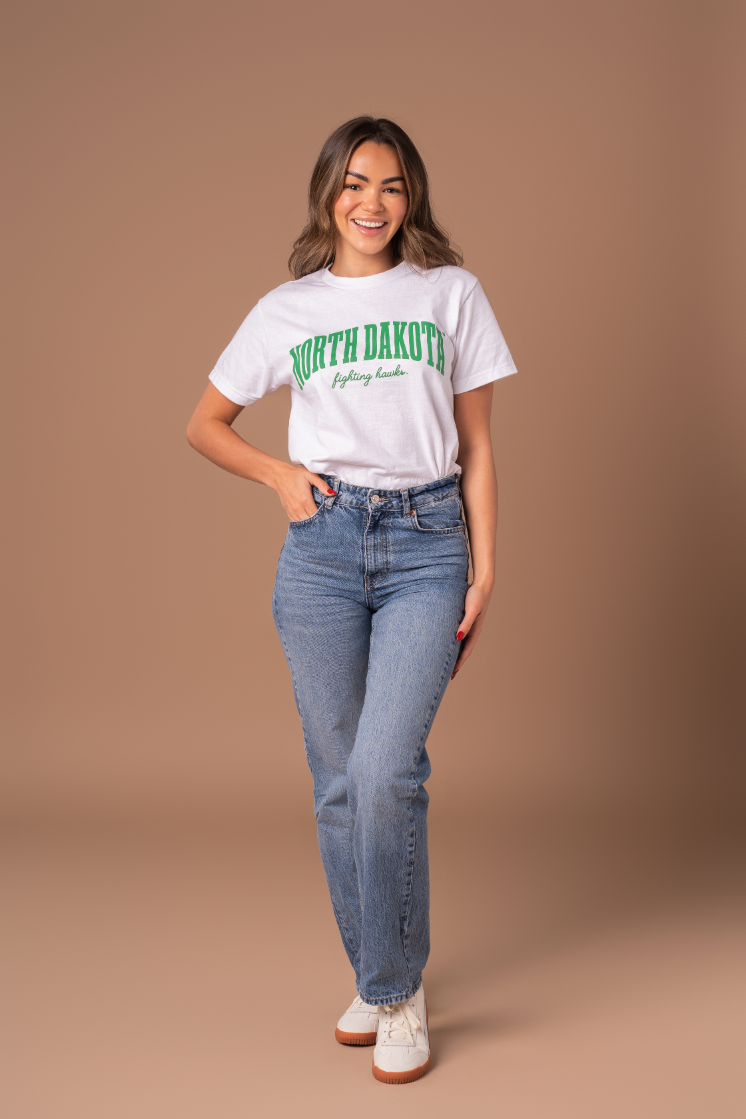 a full body image of a girl with her hand in her pocket of her jeans wearing a white tee that says North Dakota Fighting Hawks  screenprinted in kelly green