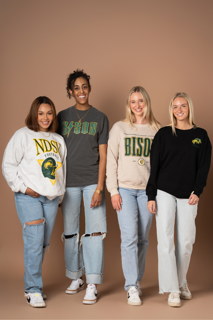 4 girls standing in a line posing with all different NDSU Bison styles on, all of which have green and gold decorations