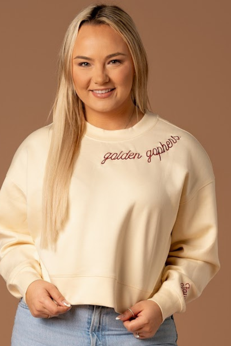 close up image of a girl wearing a bone colored supersoft crewneck with golden gophers embroidered around the collar in maroon