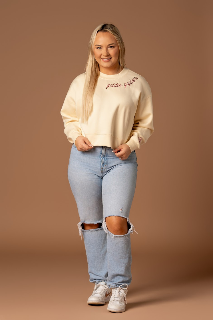 full body image of a girl wearing jeans and a black supersoft crewneck with golden gophers embroidered around the collar in maroon