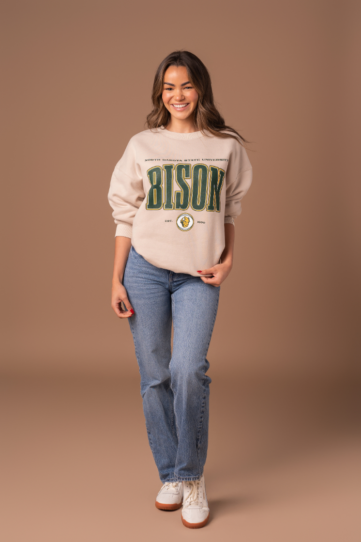 a full body image of a girl wearing jeans and a NDSU Bison crew in a tan color with green and gold screenprint