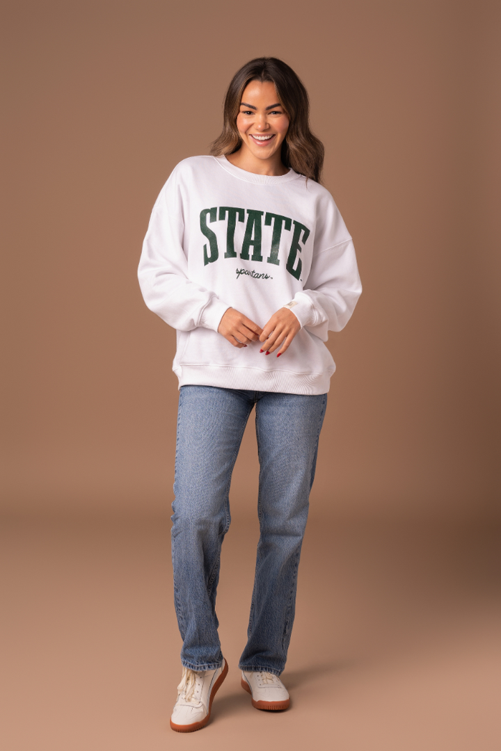 picture of a girl wearing a white Michigan State University Classic Crew Neck fleece lined sweatshirt with a green screenprinted design