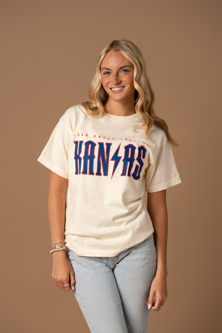 image of girl wearing a cream t-shirt with Rock Chalk Jayhawk Kansas written across the chest in red and blue with a lightning bolt graphic in the middle