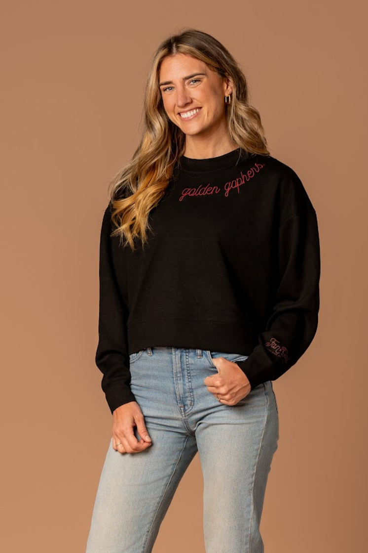 full body image of a girl wearing jeans and a black supersoft crewneck with golden gophers embroidered around the collar in maroon