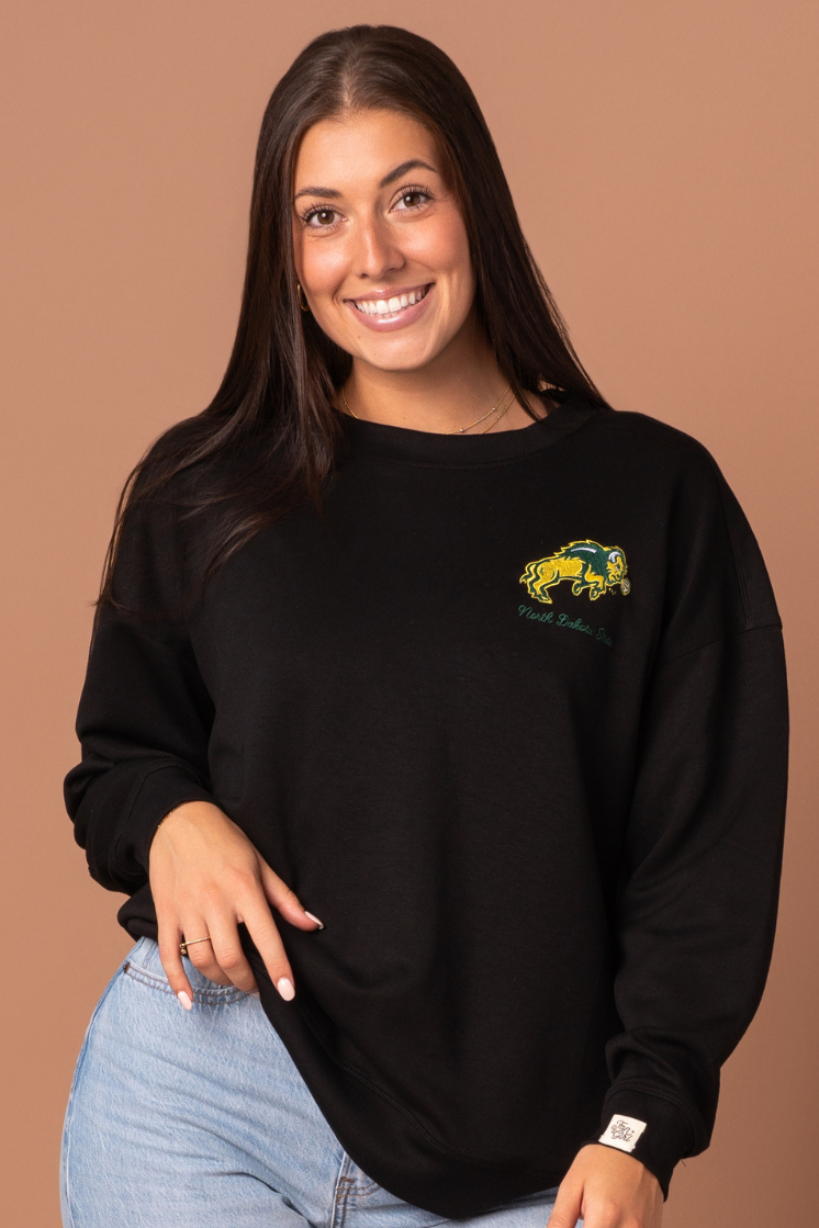 a close up of a girl wearing a black full-length crewneck with NDSU logo embroidered in green and gold on left side pocket 