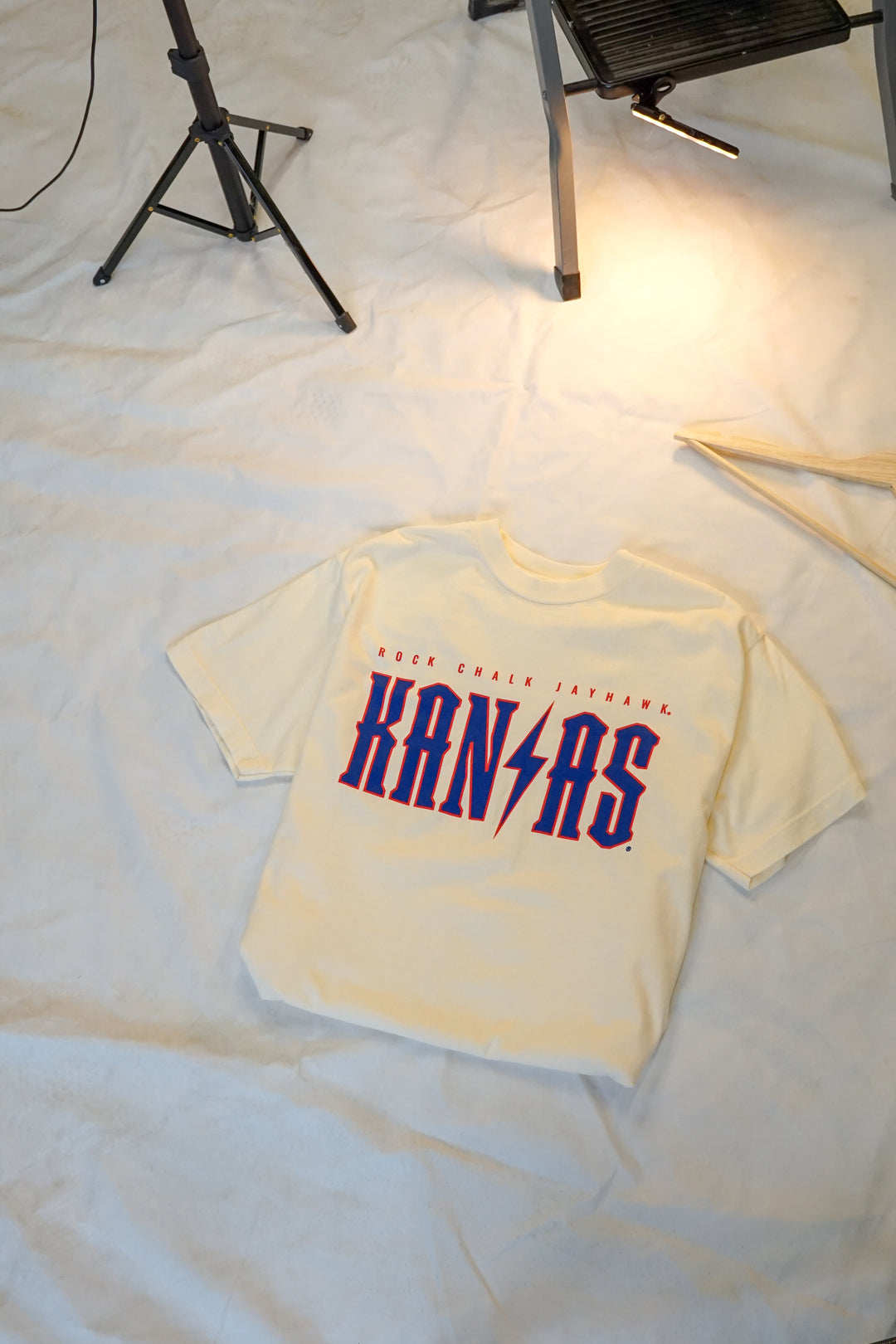 image of a flat lay cream tshirt with Rock Chalk Jayhawk Kansas written across the chest in red and blue detail