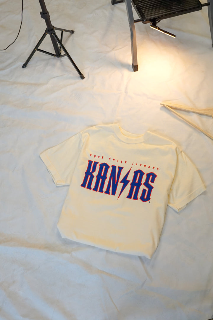 image of a flat lay cream tshirt with Rock Chalk Jayhawk Kansas written across the chest in red and blue detail