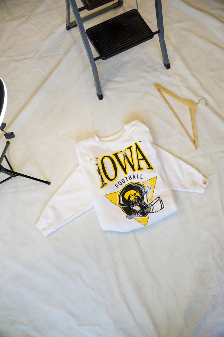 a flat lay photo of a white crew neck sweatshirt with the university of iowa hawkeyes licensed black and yellow design with a football helmet and hawkeyes logo on it.