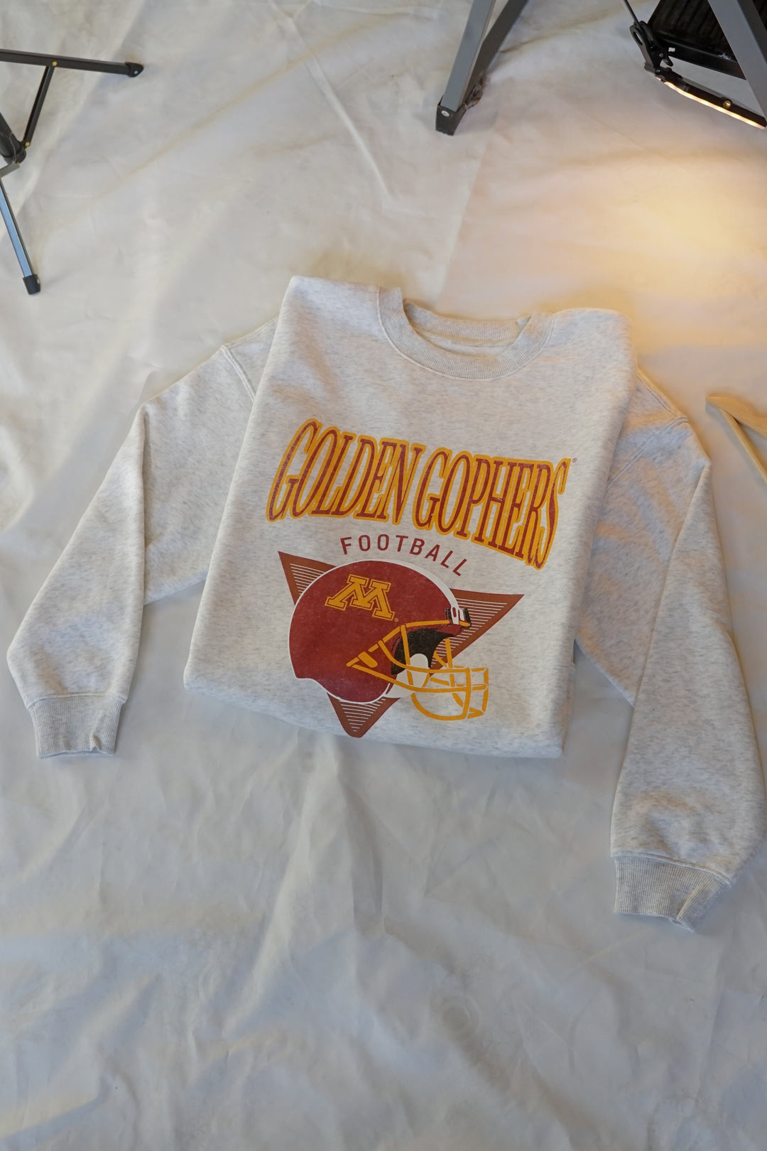 flat lay image of an ash gray crewneck with Golden Gophers Football screenprinted with a distressed football graphic in maroon and gold 