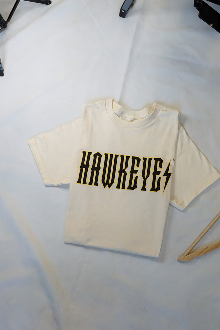 Flat laying ivory tshirt that has a trademarked Iowa Hawkeyes screenprinted design on it that resembles a trendy band tee.