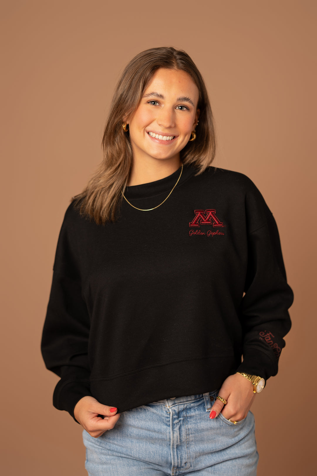 close up image of a girl wearing a black supersoft crewneck with a M logo and Golden Gophers embroidered in maroon on the left side pocket of the crew